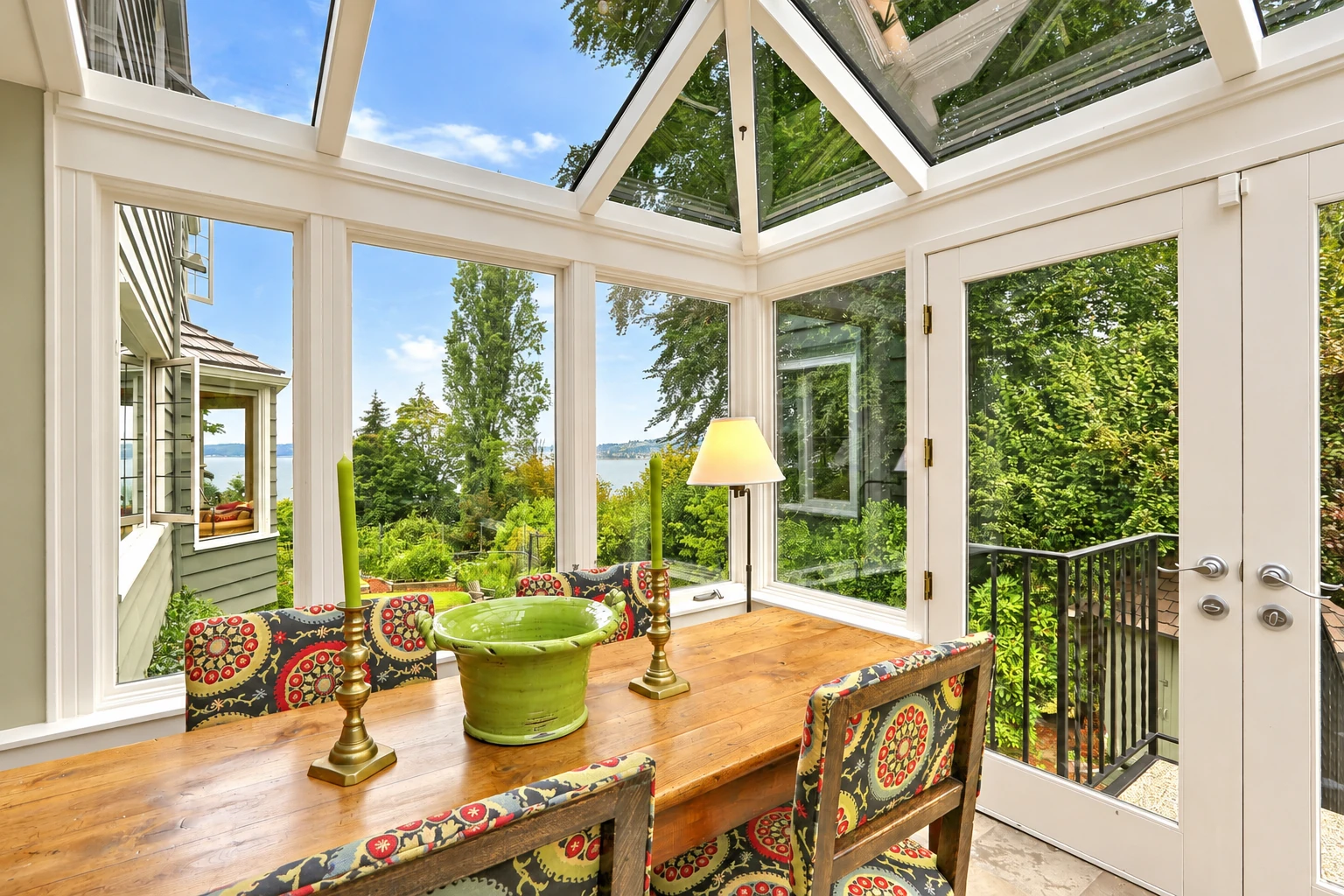 Solarium with a glass-paneled roof, white framing, and a wooden dining table surrounded by windows and greenery.