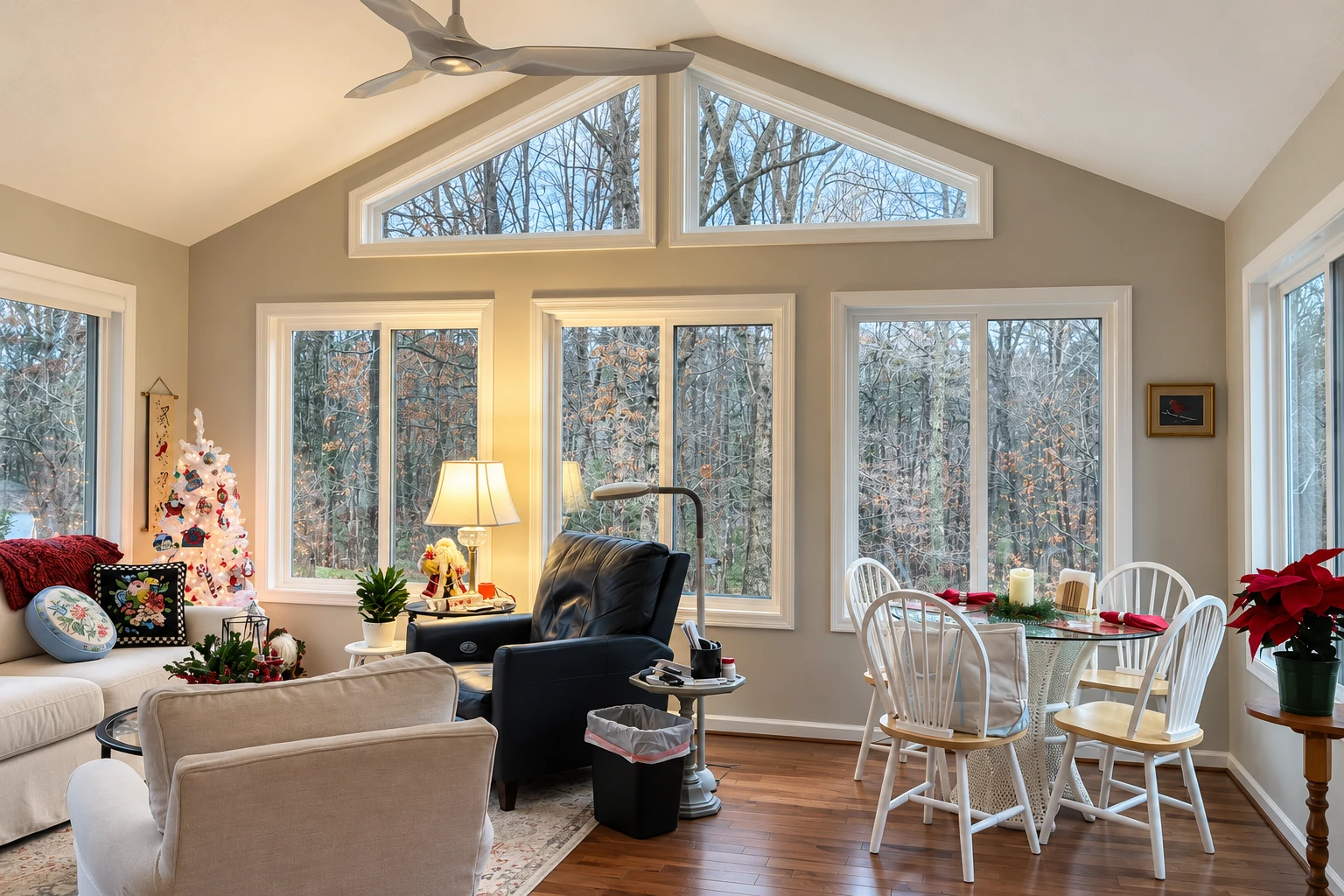 Remodeled sunroom with tall windows, vaulted ceiling, seating area, and dining table beside a winter garden.